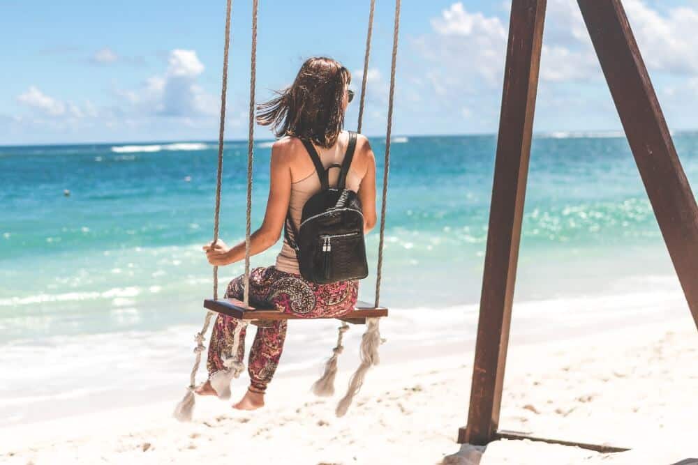 Travelling Alone While in a Relationship: Can You Do It? 6 woman on a beach swing looking out to sea.