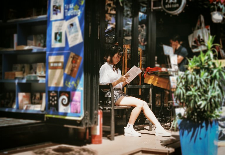 Featured image for top 10 responsible travel books to inspire your wanderlust. A girl sitting outside a shop and reading.