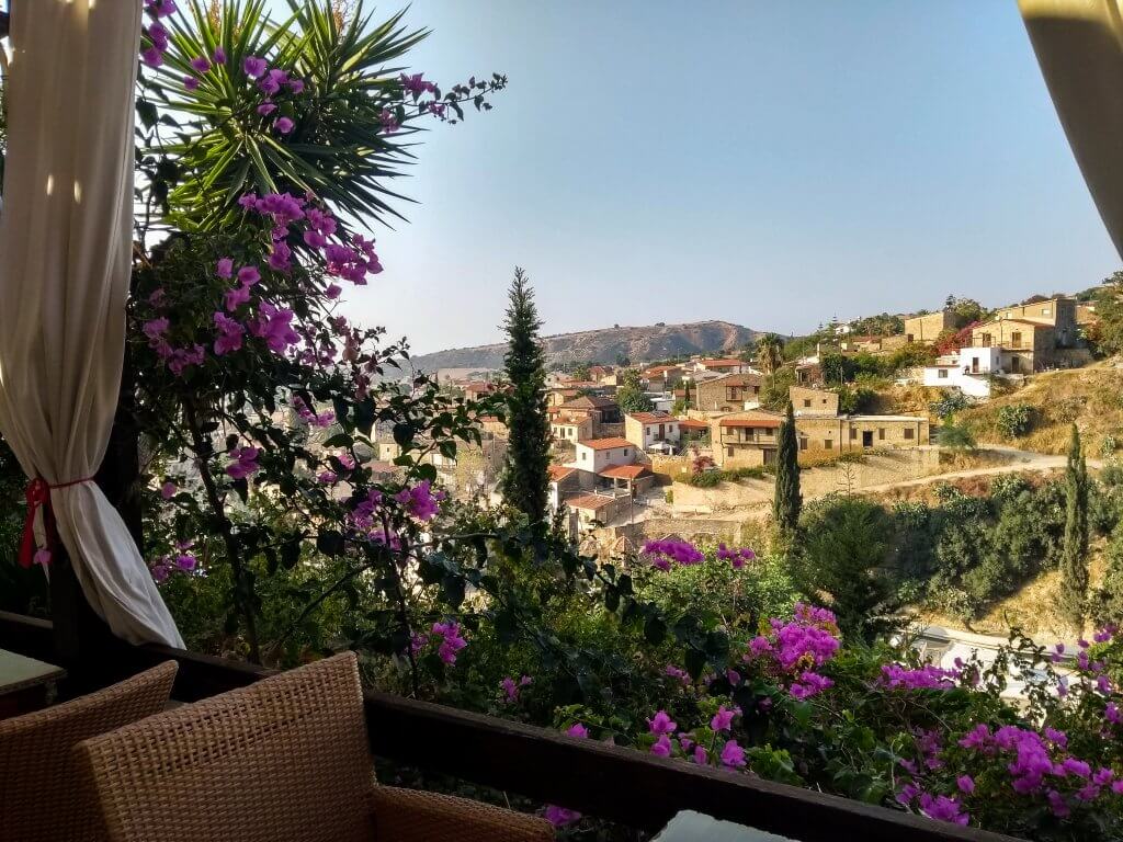 Tochni Tavern view for Cyprus itinerary. Pink flowers surround a terrace with a view of Tochni village on the hill opposite. 