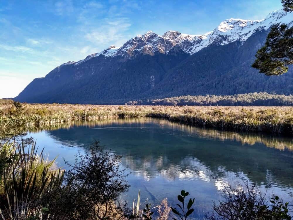 Mirror Lakes in Fiordland National Park. A lake with flatlands behind and a mountain in the distance. 