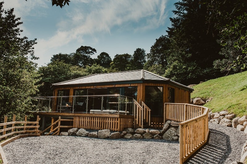 10 Sustainable Secluded Places to Stay in the UK 3 Front view of a wooden lodge surrounded by trees.
