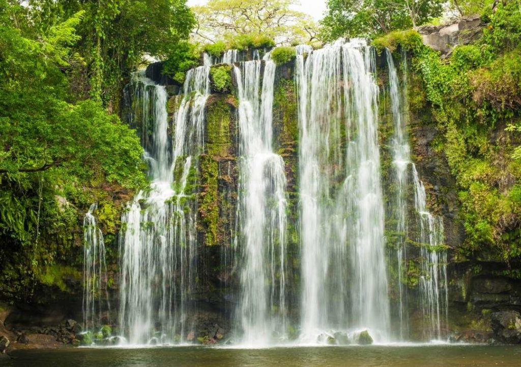A wide waterfall tumbling down a green rock face. 