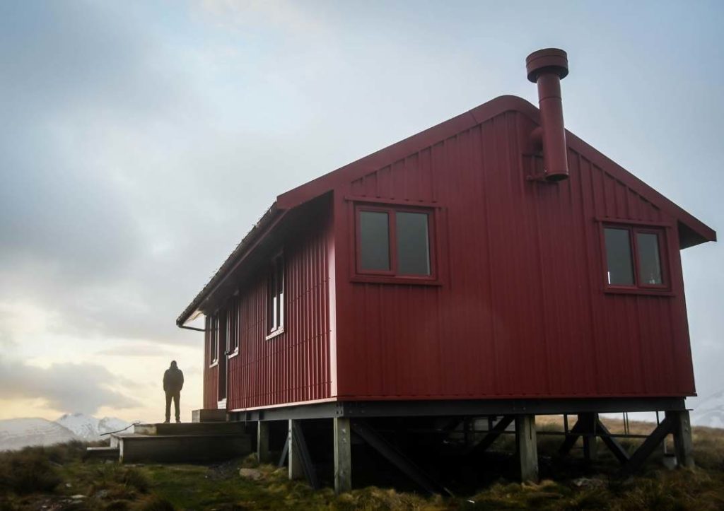 14 Incredible Hikes On the South Island of New Zealand 10 View of a big red hut with a silhouette of a person in the background at Brewster Hut.