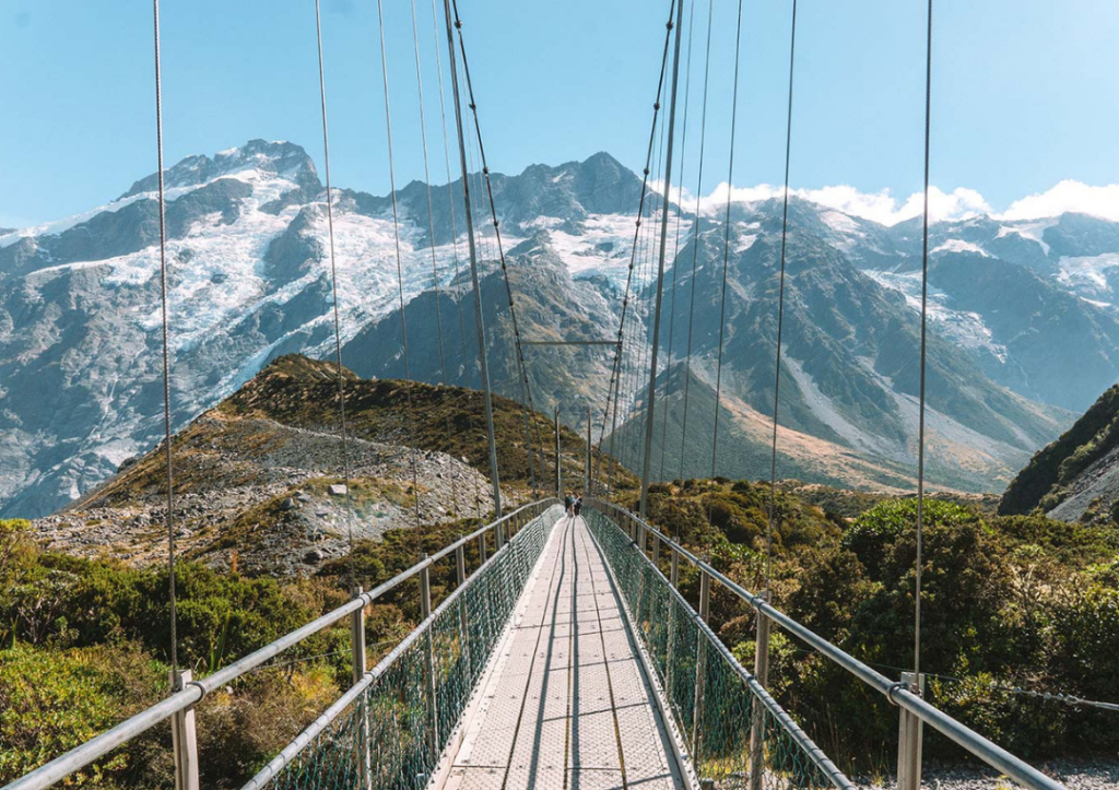 14 Incredible Hikes On the South Island of New Zealand 8 A bridge walkway with mountains behind on the Hooker Valley track, one of the best hikes on the South Island of New Zealand.