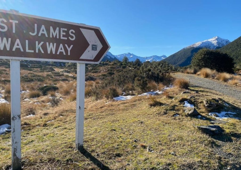 14 Incredible Hikes On the South Island of New Zealand 13 Sign pointing to the start of the trail at St James Walkway with mountains behind.
