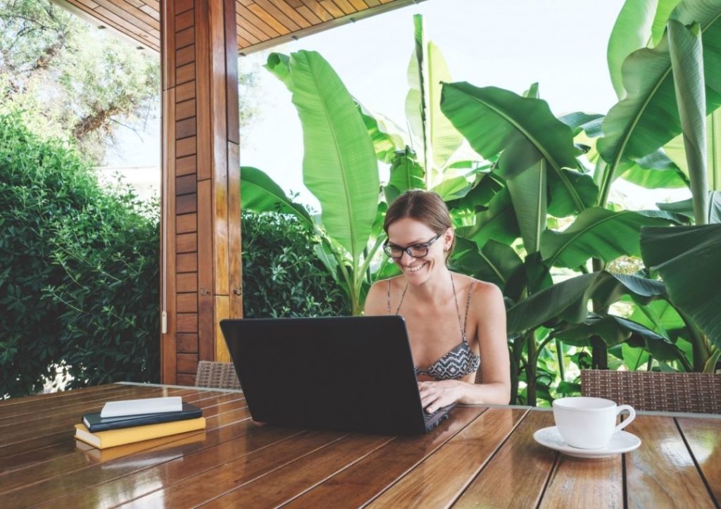 Woman on a laptop with banana tree leaves behind. 