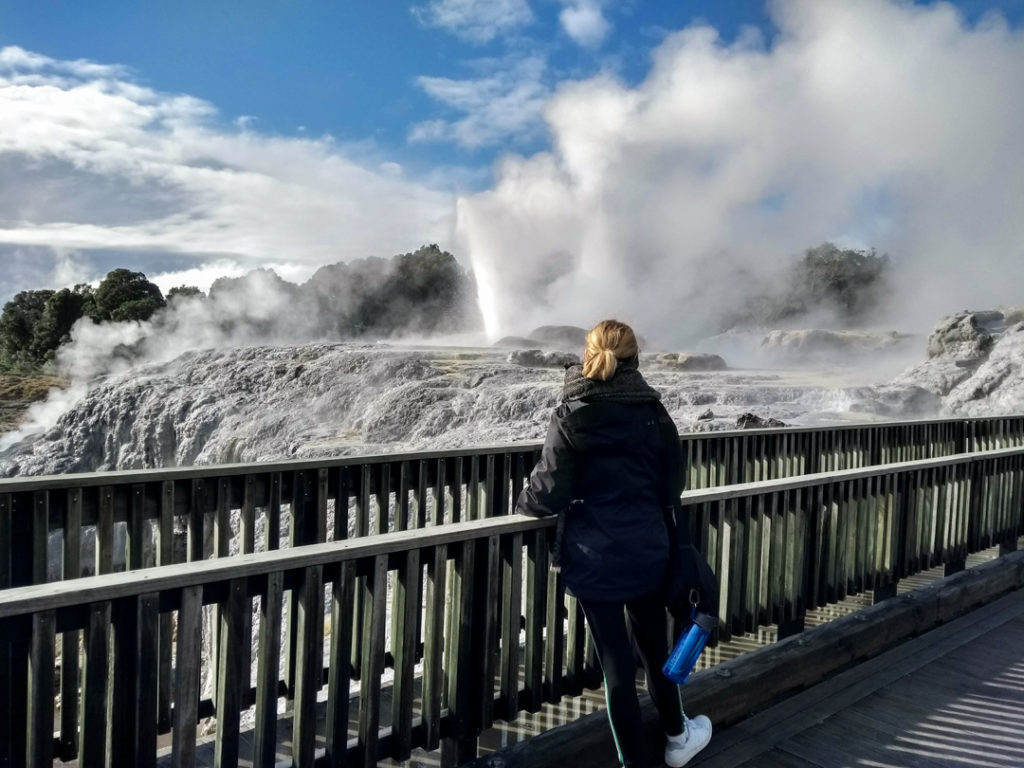 Girl with a water bottle looking at a geyser in front of her in New Zealand. 