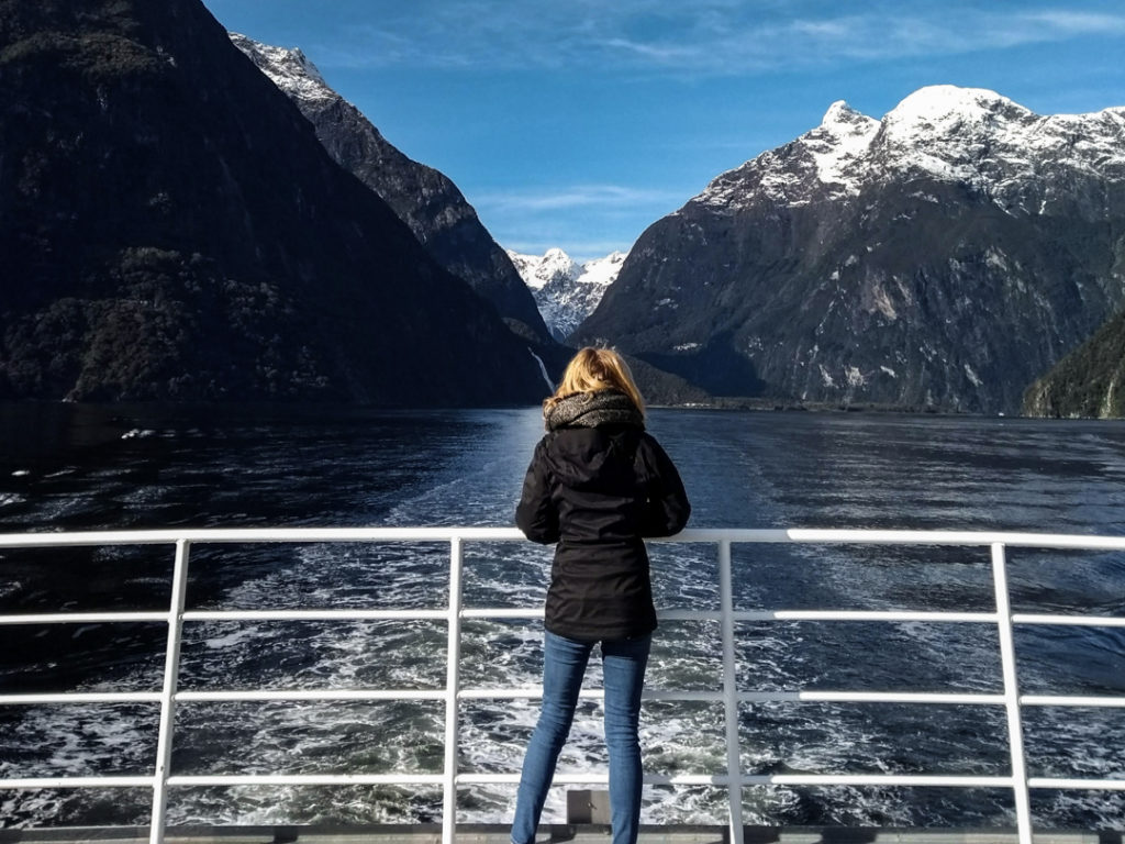 Girl on a boat with a lake behind and mountains with snow on them in New Zealand. 