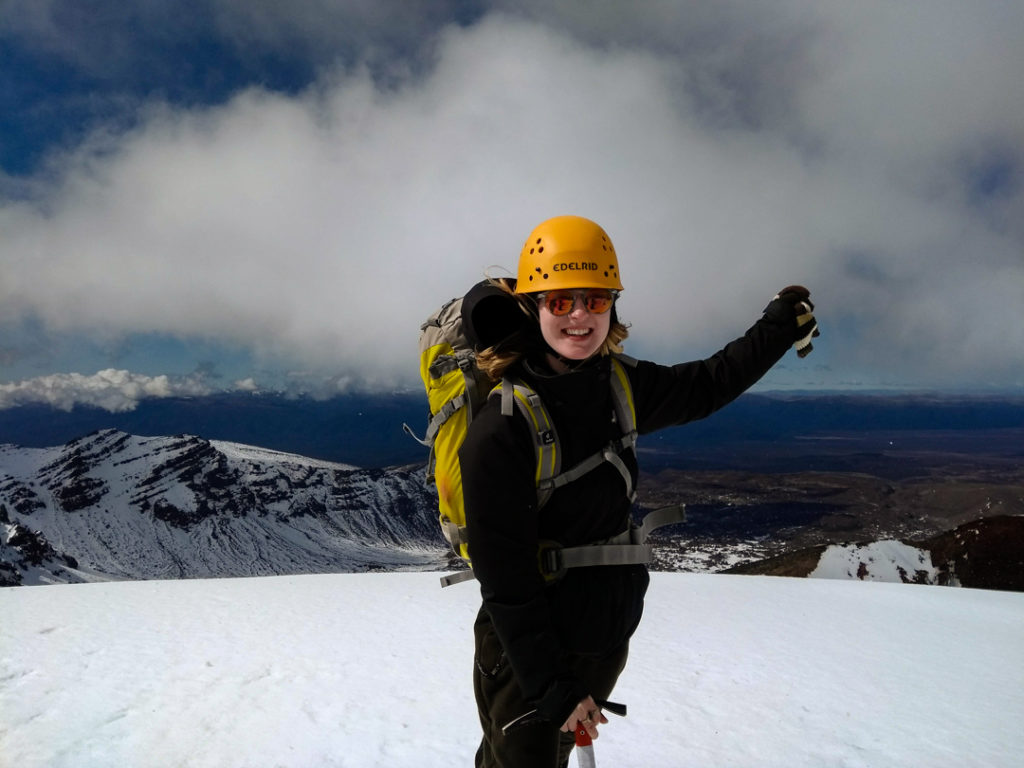 Girl in a yellow helmet and sunglasses on top of a snow-covered mountain in New Zealand. 