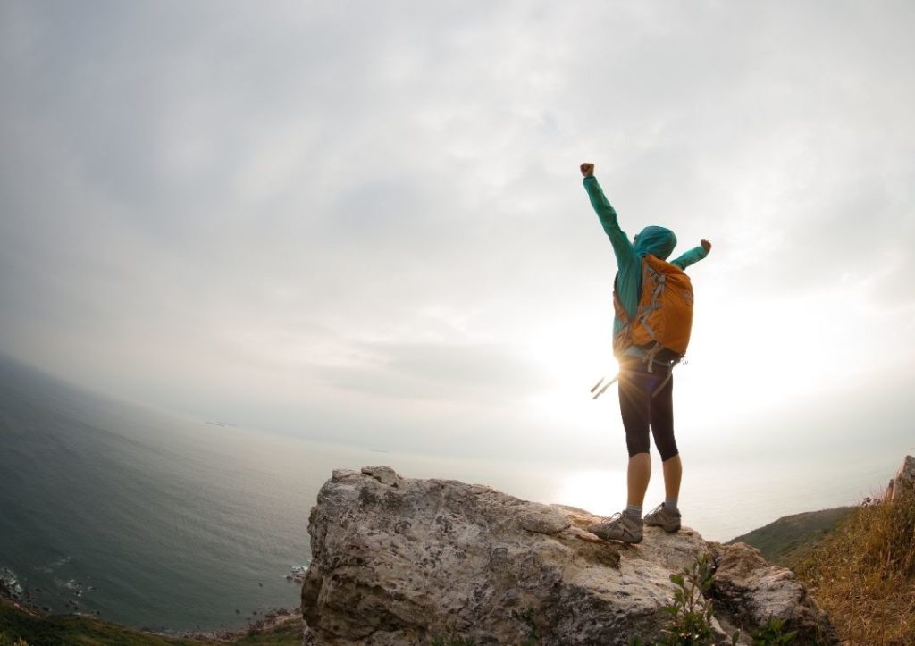 Hiker standing on a rock with their arms up for eco-friendly ways to travel. 