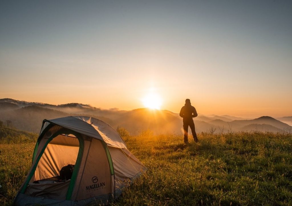 Person with a tent watching the sun rise over misty hills. 