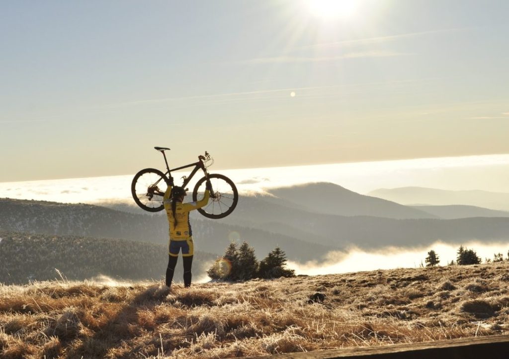 Cyclist holding up a bike in the hills at sunrise. Cycling is one of the best eco-friendly ways to travel. 