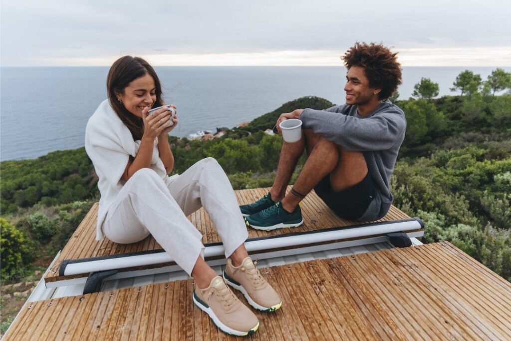 Two people wearing Tropicfeel sneakers sitting on a wooden roof with mugs in their hands. 