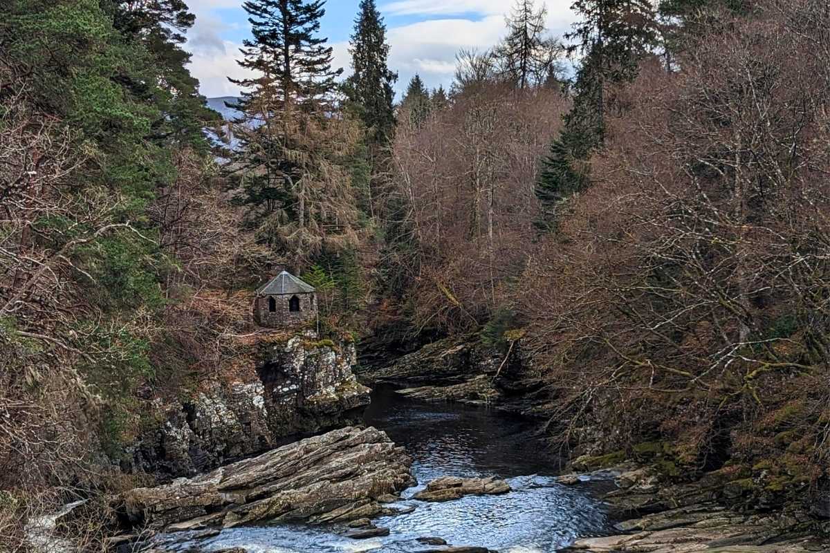 A secluded stone lookout structure perched on a rocky ledge above the River Moriston, surrounded by dense woodland in Invermoriston, Scotland. A peaceful stop on the best Scotland day tours, this hidden gem offers scenic views and tranquil forest trails.