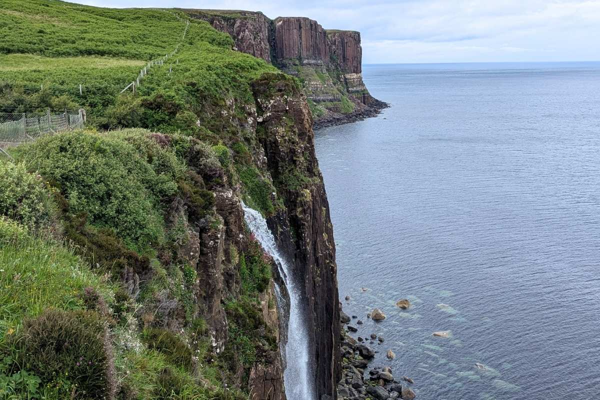 The dramatic Kilt Rock cliffs on the Isle of Skye, with a waterfall cascading down into the ocean below and rugged, vertical basalt columns rising above the sea.