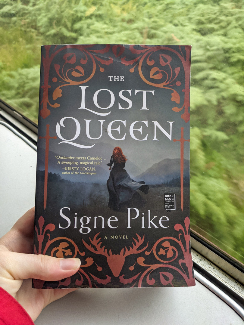 Jacobite Steam Train Review: What It's Really Like (+ Photography Tips!) 3 A hand holding a book with a girl on the cover - The Lost Queen by Signe Pike.