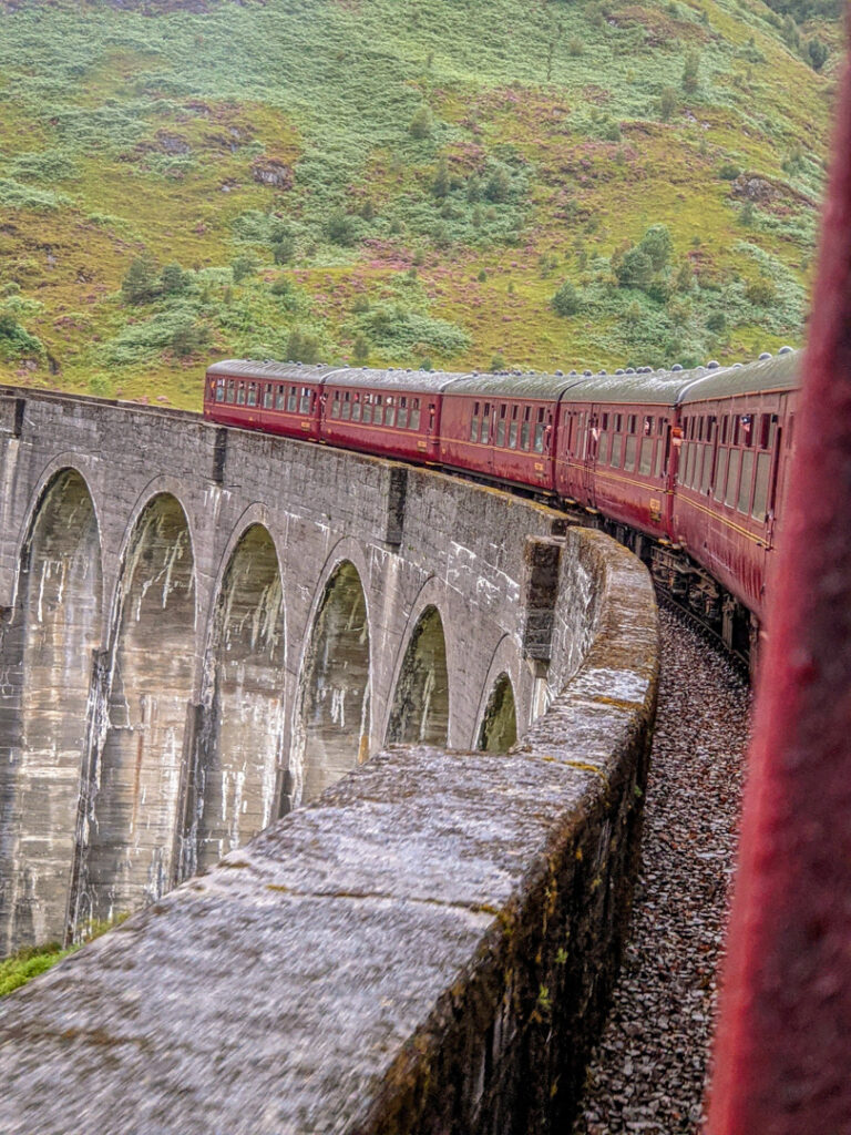 Red train carriages going over Glenfinnan Viaduct. 