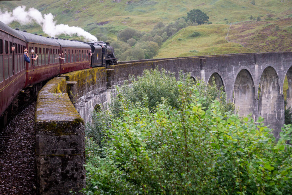 Red steam train going over Glenfinnan viaduct.