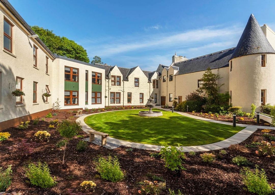 White building with big windows and a large garden space. Cuillin Hills Hotel is one of the best places to stay on Skye. 