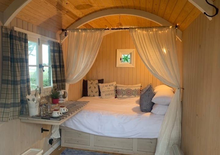The inside of Loch Eyre Shepherds Hut. A bed with a curtain and fairy lights. 