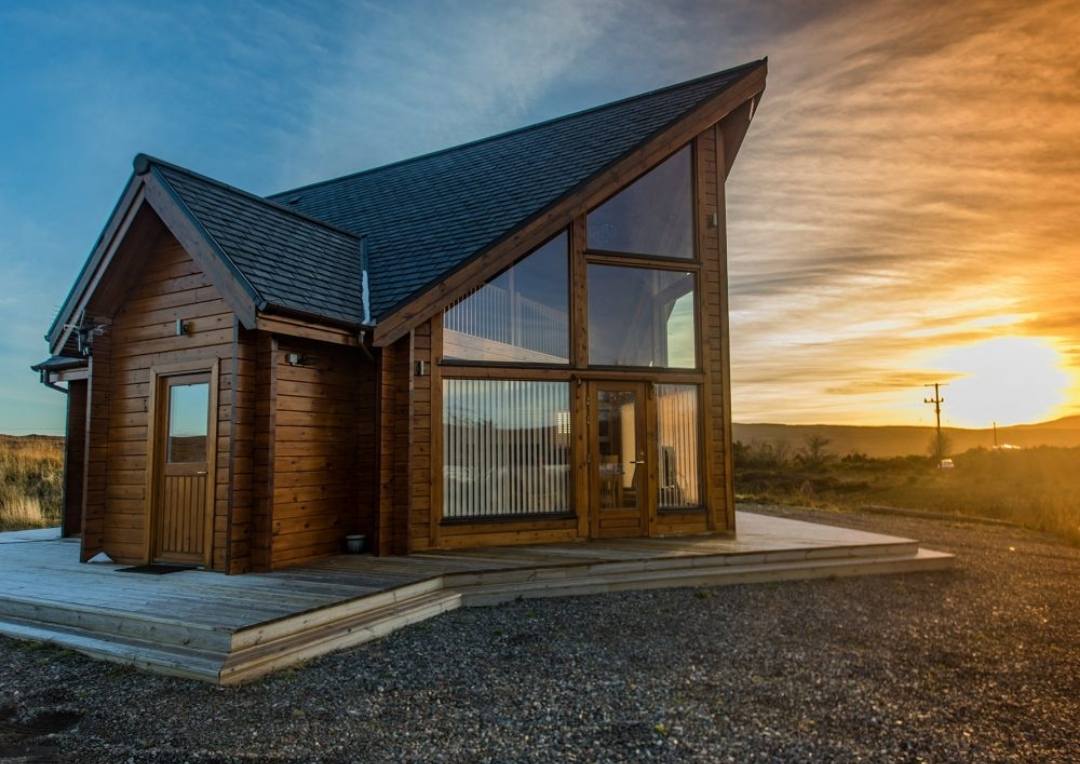 A wooden lodge with large glass windows at sunset on the Isle of Skye. 