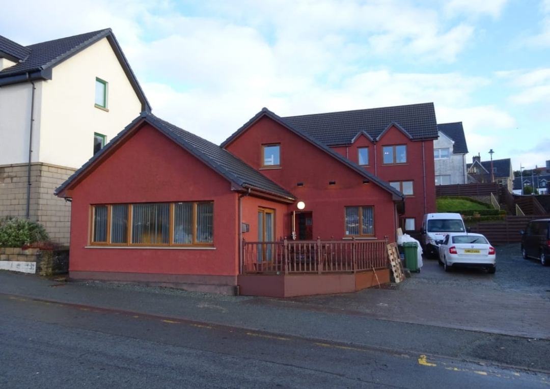 A red painted building with white cars next to it for Portree Youth Hostel. 