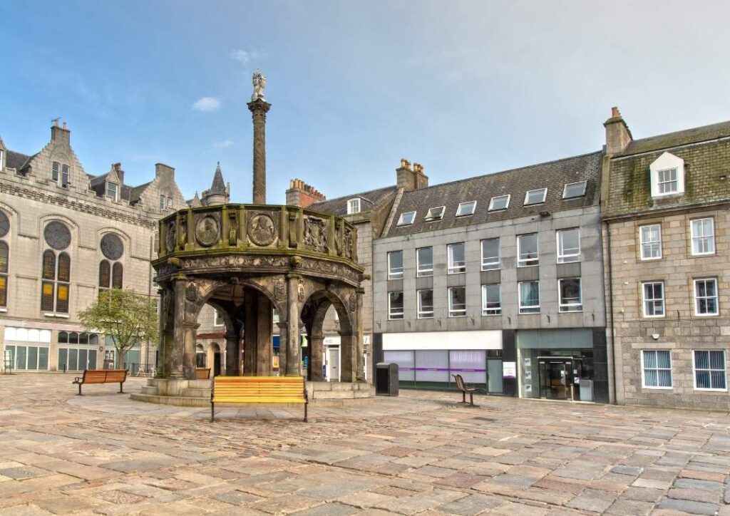A square in Aberdeen with a monument in the middle and surrounding buildings. 