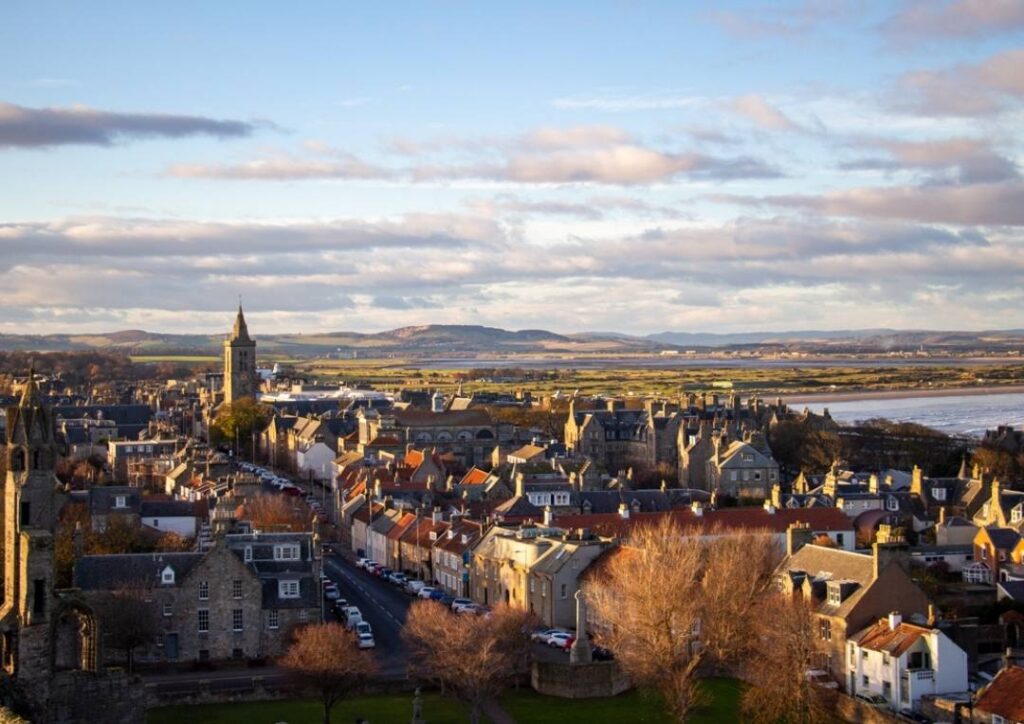 View of St Andrews in Scotland from above. The cathedral and red roofed houses with hills behind. 