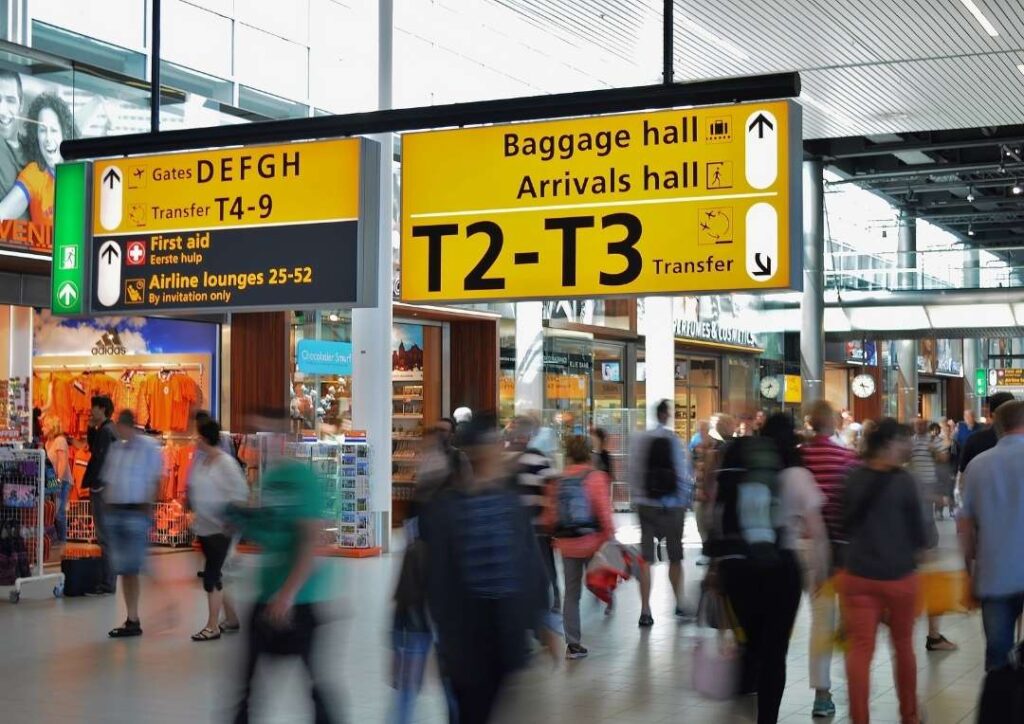 Signs at an airport with blurred people walking underneath them. 