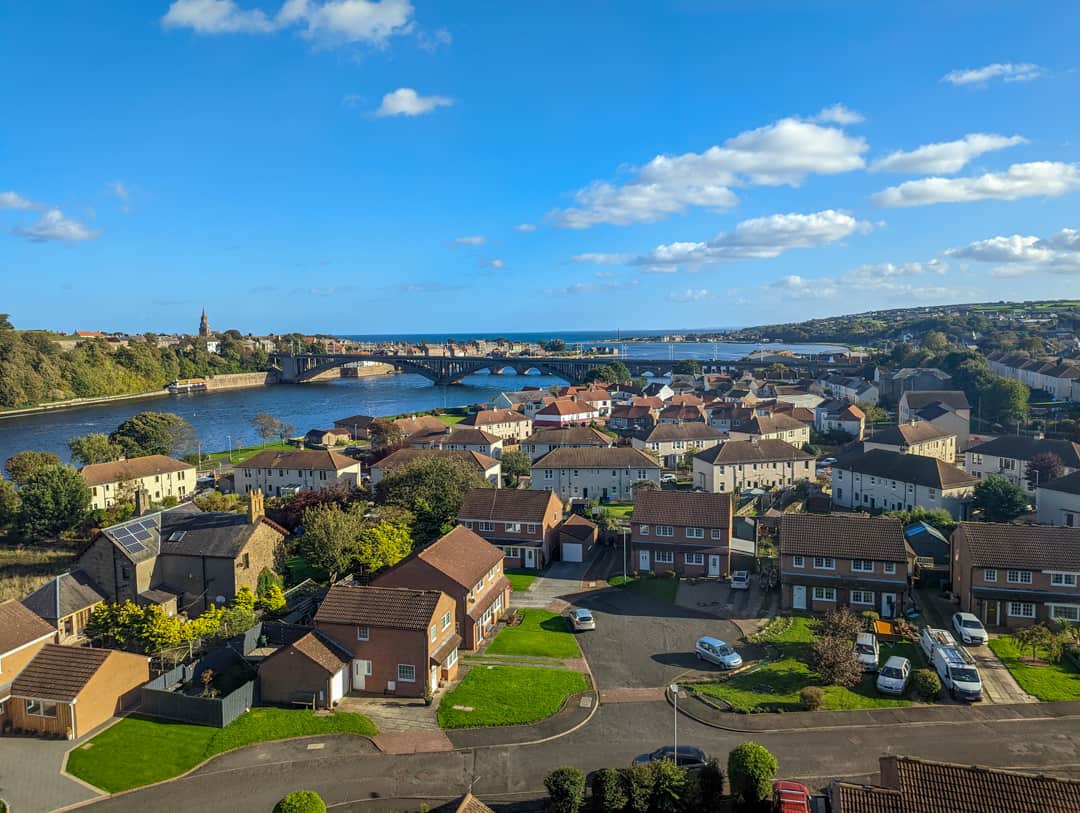 View of the Scottish Borders from the train. Houses in the foreground and a river with a bridge. 