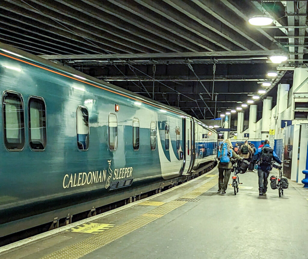 The Caledonian Sleeper Train at the platform at Euston Station, London. Passengers with bikes walking up ahead, 