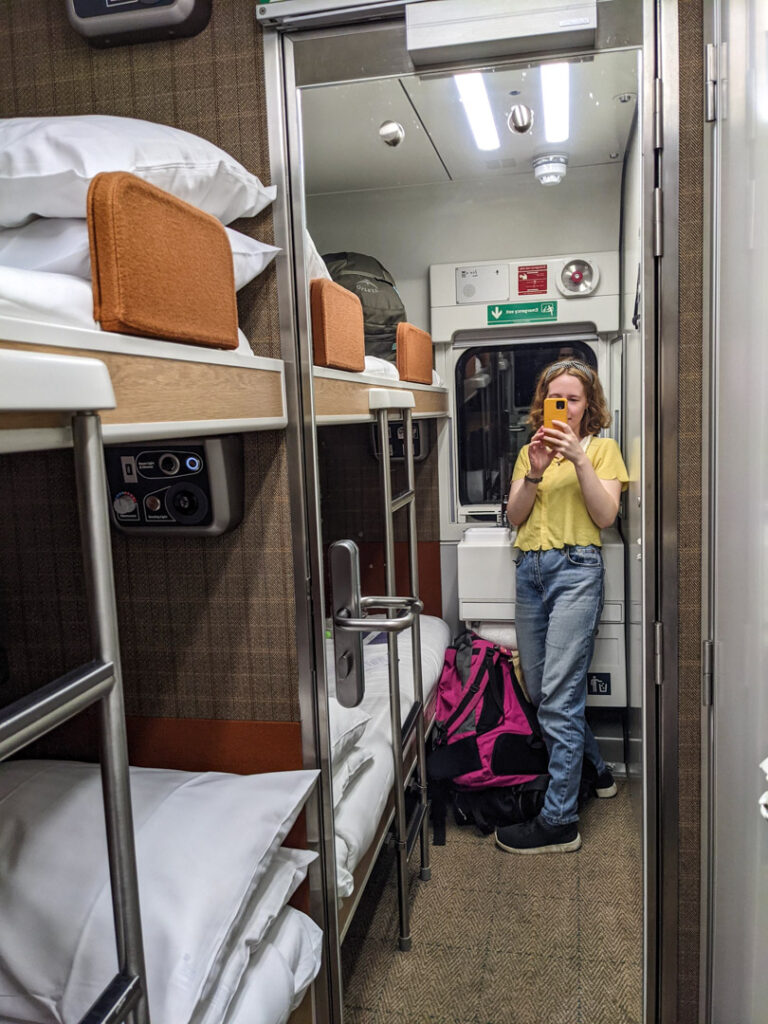 Inside the Caledonian Sleeper Classic Room. A girl takes a picture in the full-length mirror beside a bunk bed. 