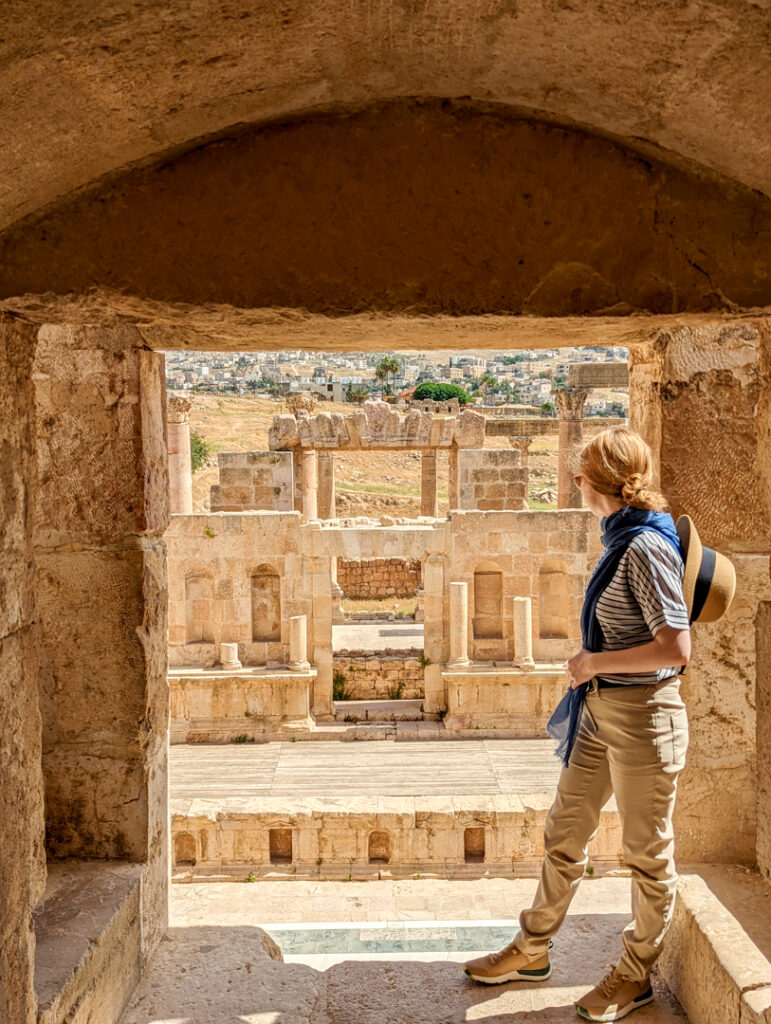 The Best Jordan Packing List: All The Essentials You Need in 2024 6 A girl in desert trousers and striped top with a blue scarf and sun hat looking down onto Roman ruins at Jerash.