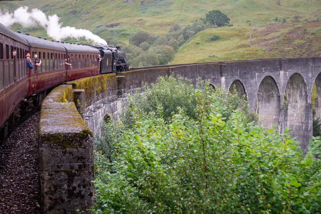 View from a red steam train (the Jacobite) going over the cement arches of Glenfinnan Viaduct in Scotland. 