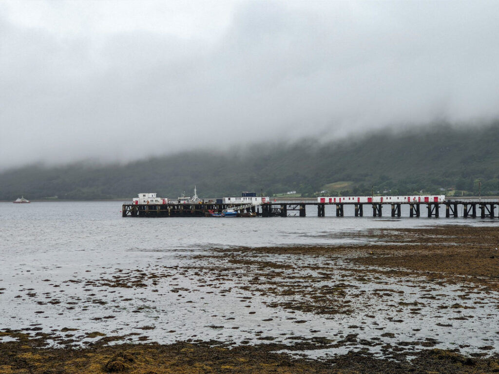An overcast day with clouds descending over a loch and a jetty sticking out from the shore. Loch Linnhe in Fort William. 