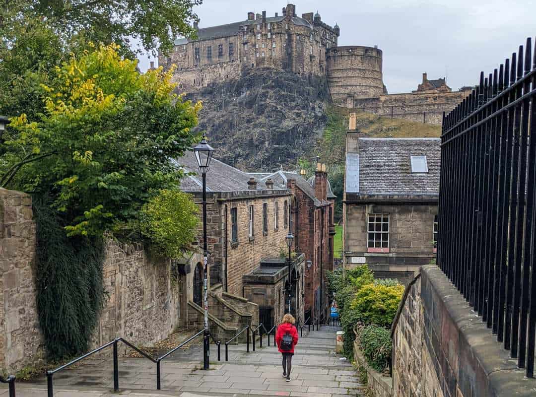 11 Best Day Trips From Glasgow By Public Transport 2 A girl in a red jacket walks down stone steps with a view of Edinburgh Castle perched on the crags above. The Vennel in Edinburgh.
