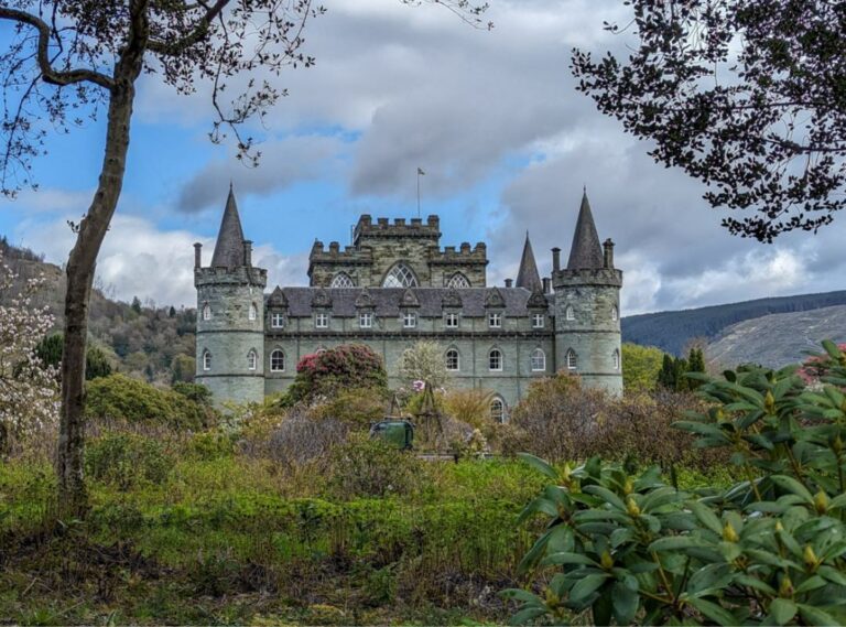 A large ornate catle sits in a green garden. There are two turretted towers on either side of it and a crenelated tower in the centre. Inveraray Castle.