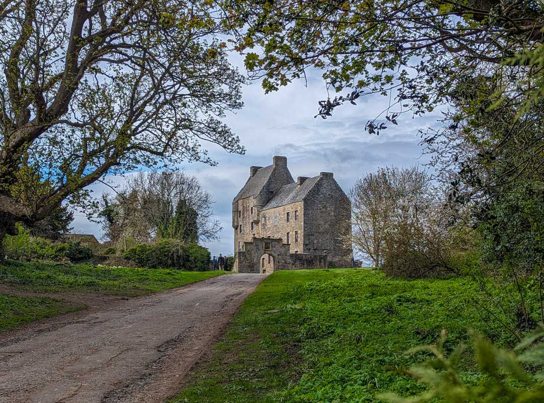 11 Best Day Trips From Glasgow By Public Transport 12 A tall hunting lodge castle with an ornate stone arch entrance sits at the end of a track surrounded by grass and trees. Midhope Castle in Scotland.