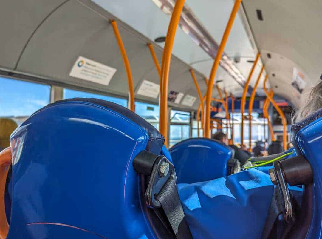 Inside a regional bus in Scotland. The back of blue seats with orange poles in the bus. 