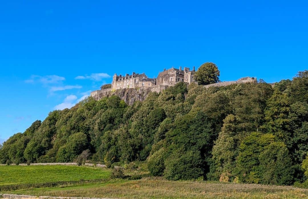 11 Best Day Trips From Glasgow By Public Transport 5 A castle sits on a crag surrounded by green trees with a bright blue sky behind. Stirling Castle, Scotland.