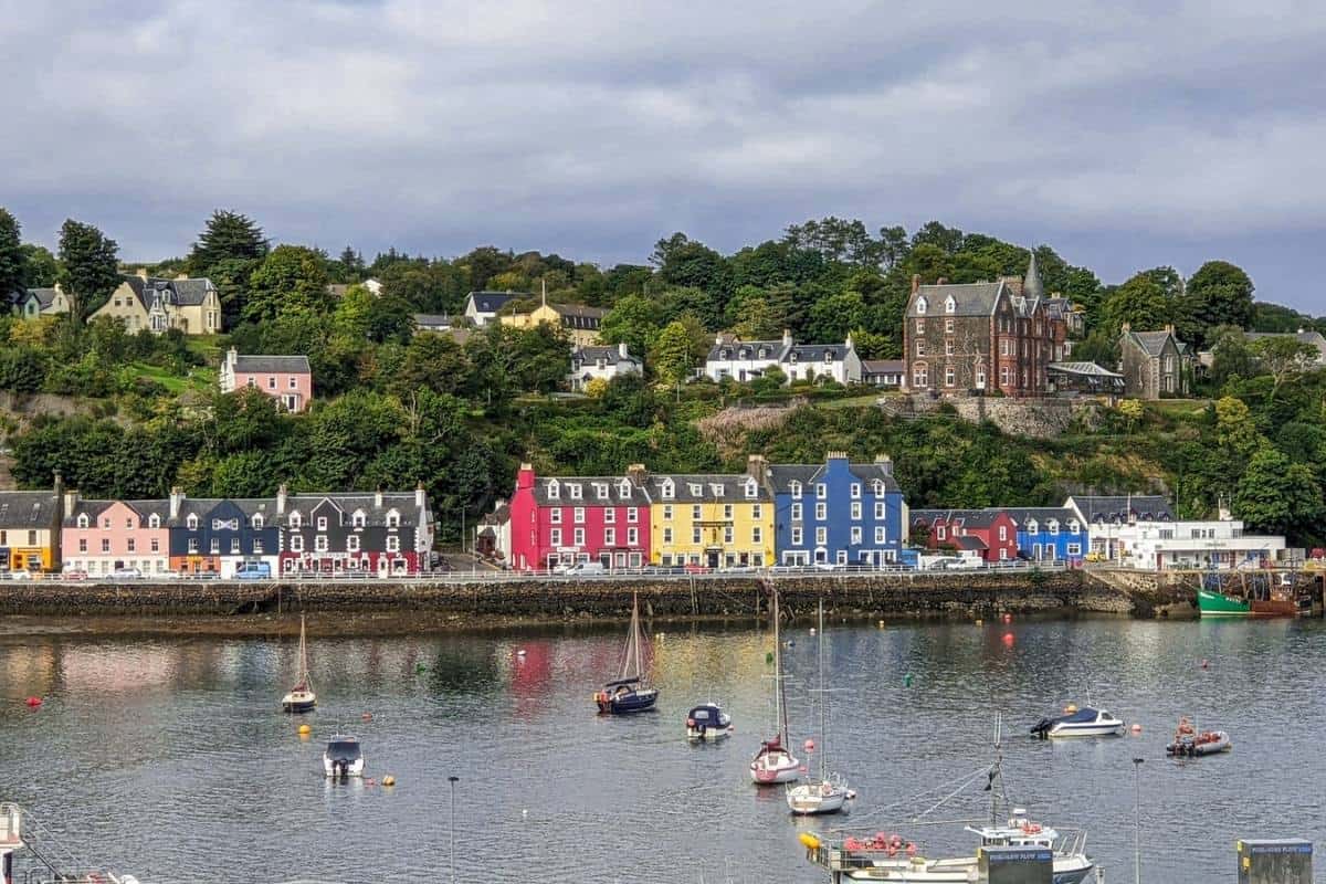 View from across a harbour at colourful houses. Boats bob on the water. Tobermory on the Isle of Mull. 