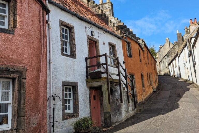 17 Best Towns to Visit in Scotland Without a Car 1 Narrow cobbled street lined with centuries-old cottages in pastel shades in Culross, their steep roofs and stone steps showing historic charm.