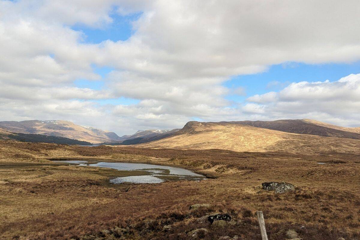 13 Best Places to Visit in Scotland by Train 1 Rolling hills and a small loch under a cloudy sky in Corrour, one of the best places to visit in Scotland by train for dramatic scenery.