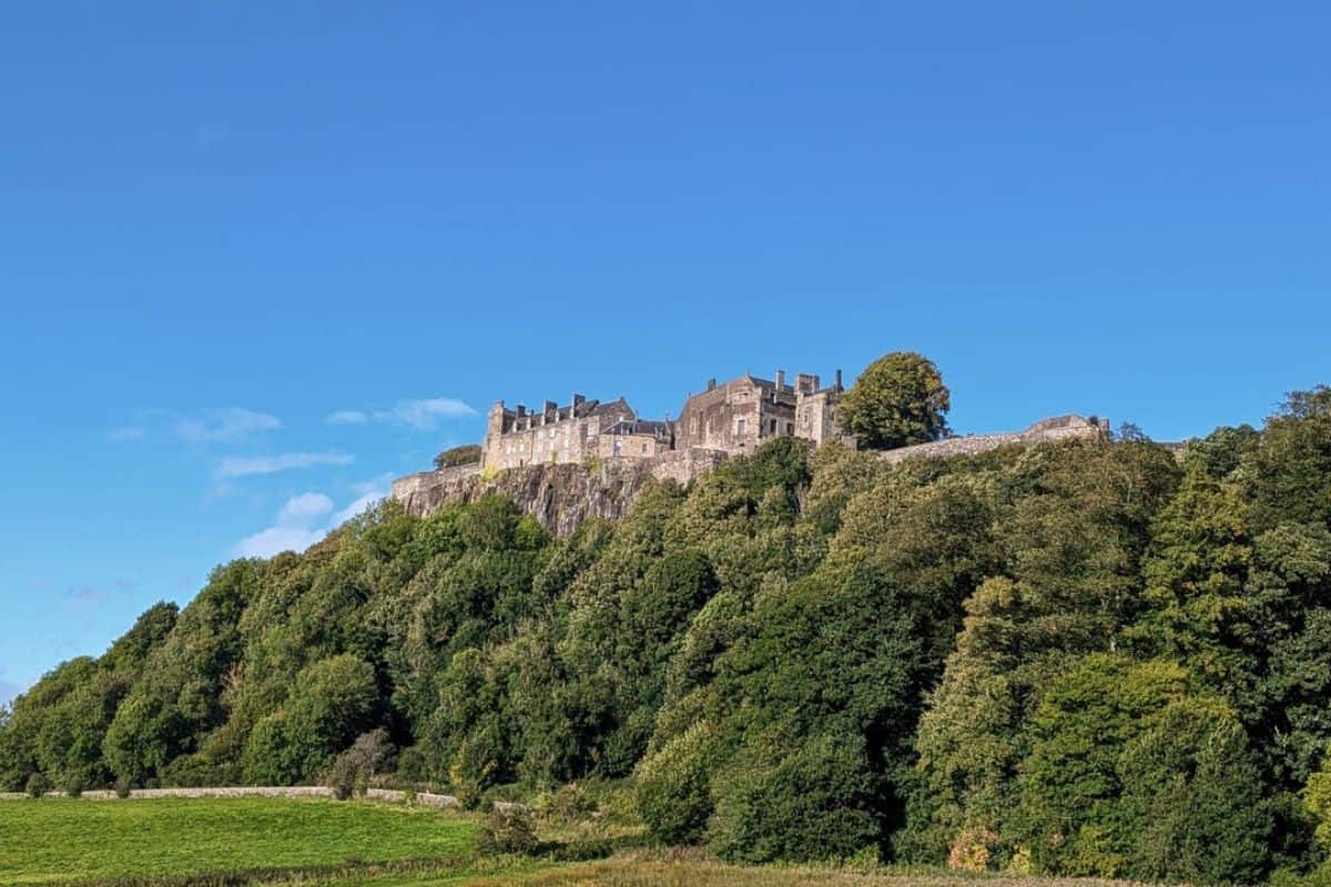 13 Best Places to Visit in Scotland by Train 12 View of Stirling Castle on the rocky crags surounded by green trees.