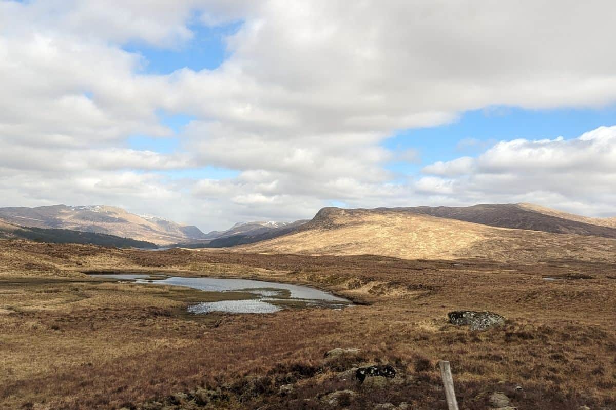 7 Most Scenic Train Journeys in Scotland with Epic Views 3 The vast moorlands of Rannoch Moor with a small loch in the middle ground. Mountains are in the distance, covered with snow. View from the West Highland Line.
