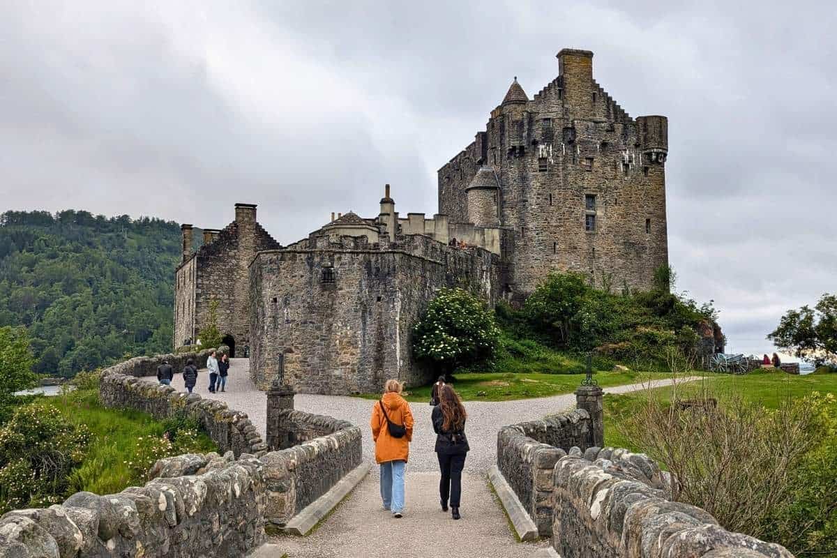People are walking up to and taking photos of the outside of Eilean Donan Castle, one of the stops on a tour. 