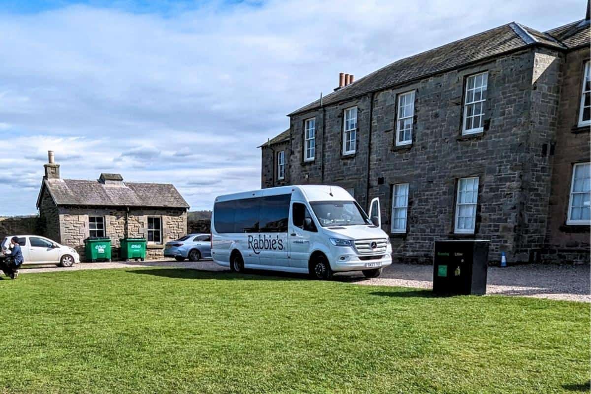 White Rabbie's minibus parked beside a lawn next to a dark brick building for this Rabbie's tours review. 