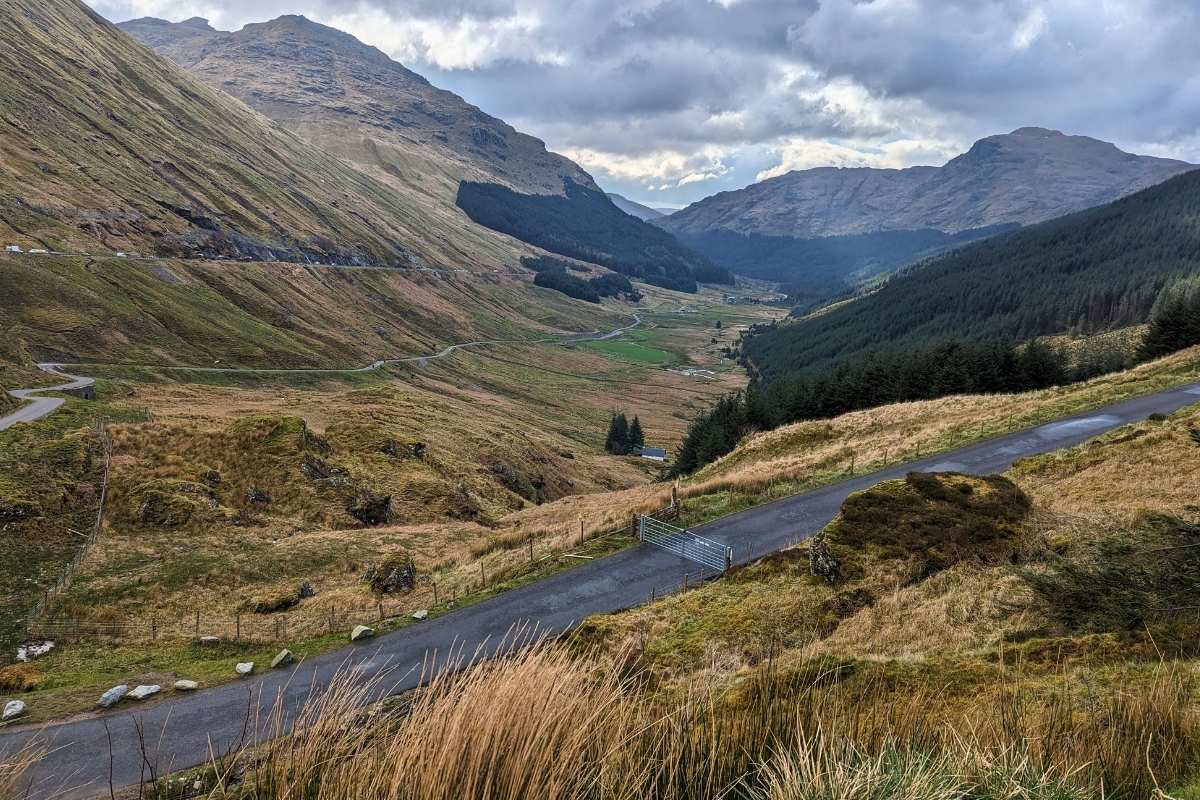 The Rest and Be Thankful Viewpoint on this Rabbie's tours review. Roads wind along a glen with trees and it's a cloudy day. 