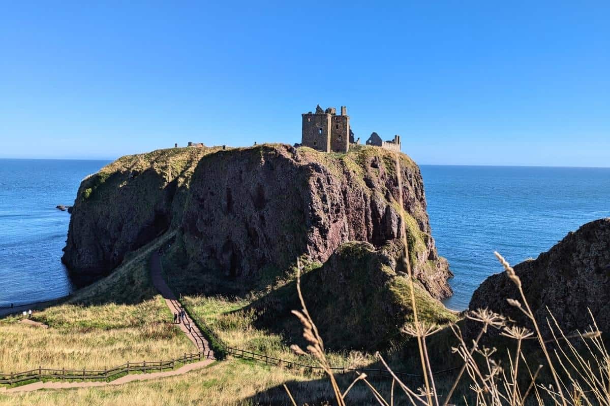 Image of Dunnottar Castle in the blazing sunshine on a cloudless day. The blue North Sea behind. It's one of the best day trips from Edinburgh by train or bus. 