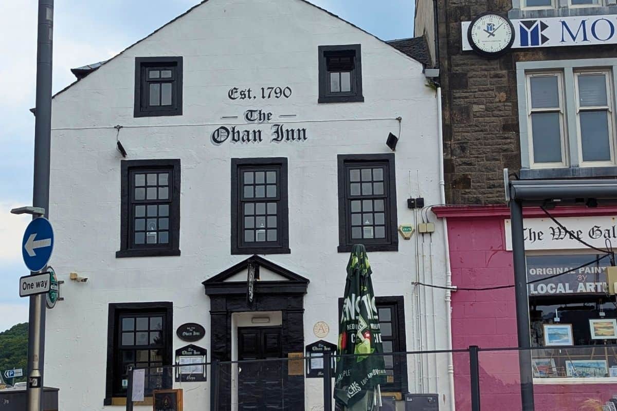 A three-storey whitewashed building with black framed windows and a door. The words 'The Oban Inn, est 1790' are above it. 